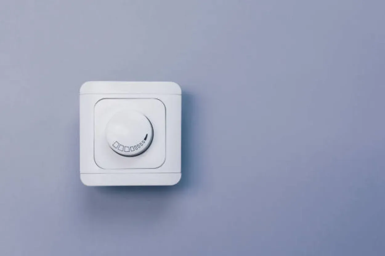 A dimmer switch with a knob attached to a cyan colored wall