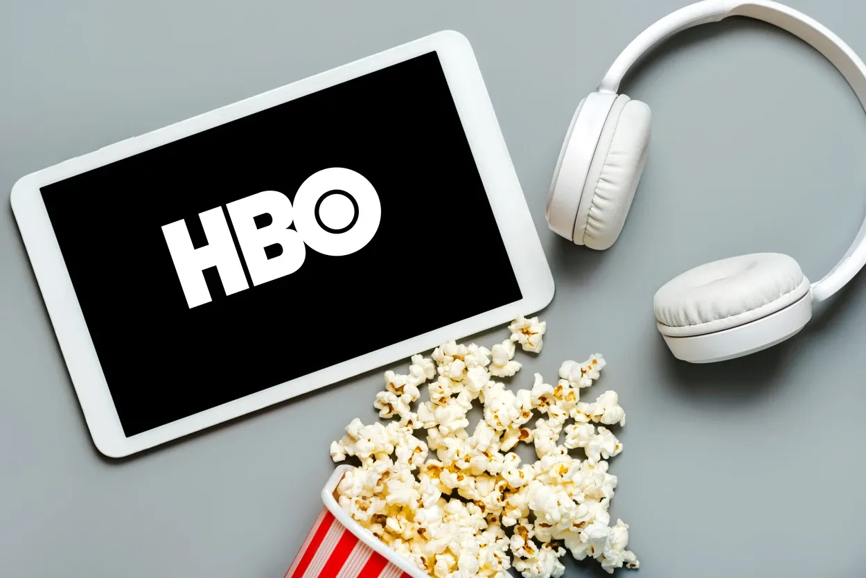 HBO logo on the screen of a white digital tablet with popcorn and white headphones on a gray background