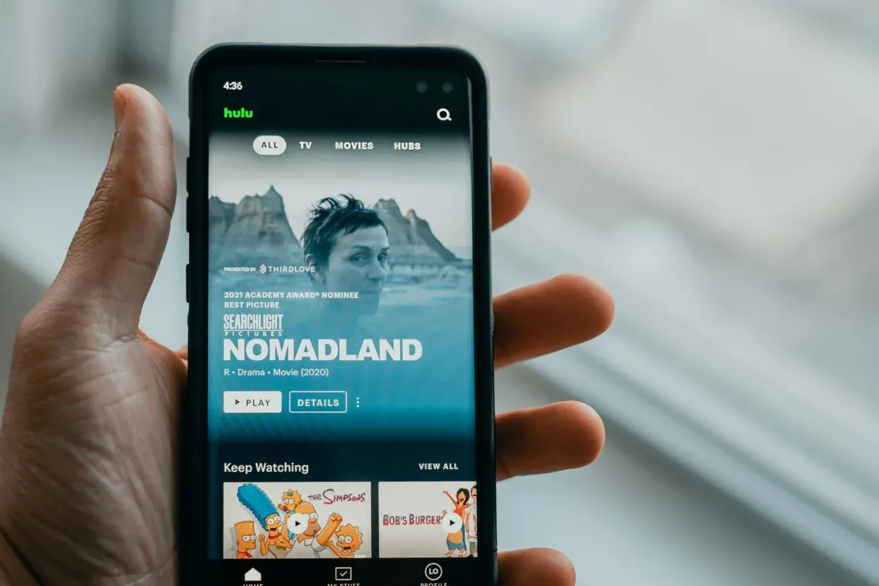 A person holding a phone displaying the Home page of Hulu