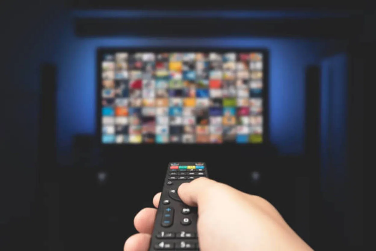 Multimedia video concept på TV i mörkt rum. Man tittar på TV med fjärrkontrollen i handen.