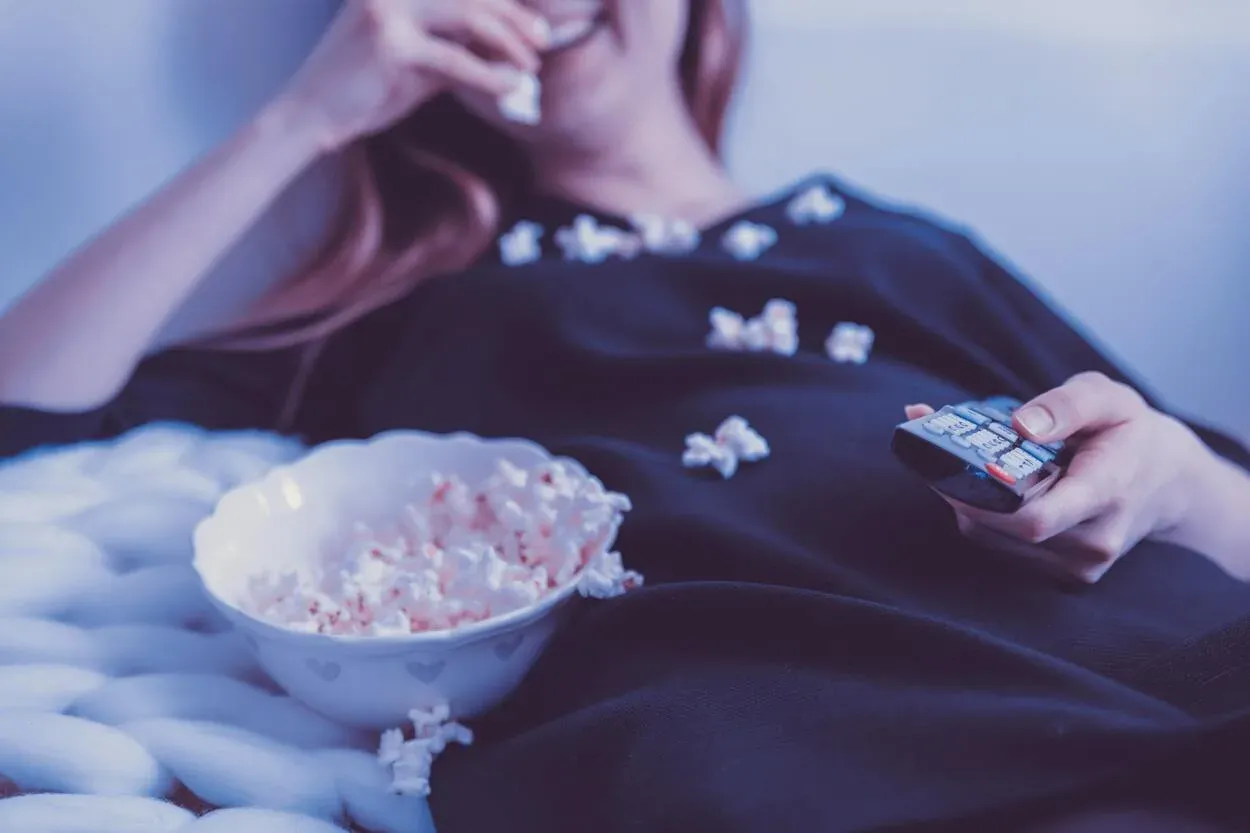 A person watching TV and eating popcorn