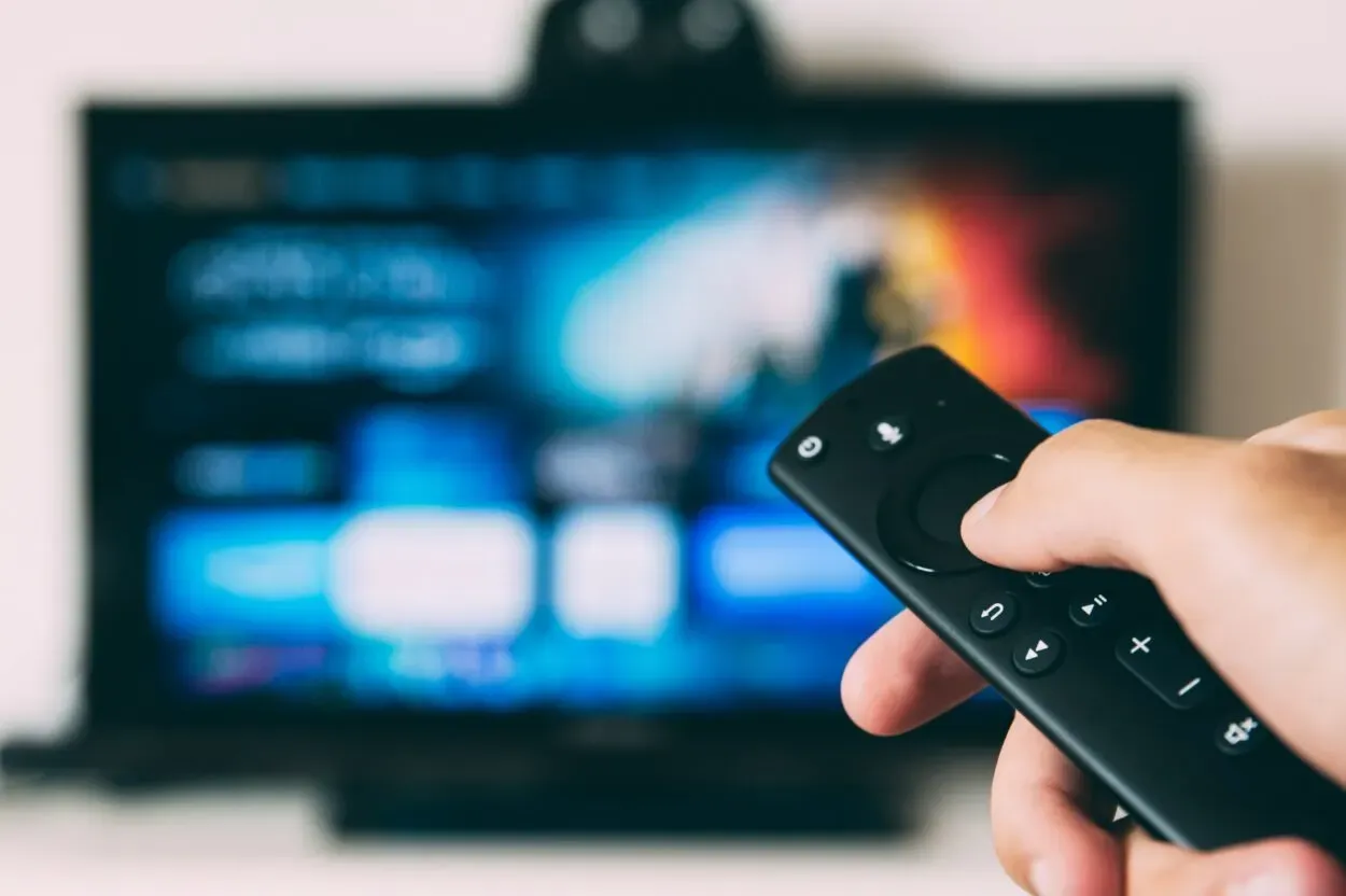 A person holding the remote and pointing it towards a TV