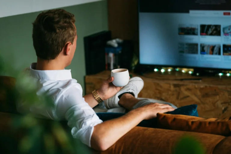 Un hombre con camisa blanca que sostiene una taza viendo la televisión
